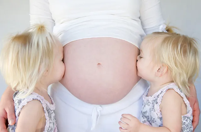 Zwei Kinder küssen den Bauch ihrer schwangeren Mutter